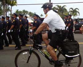 office on bicycle next to marching officers
