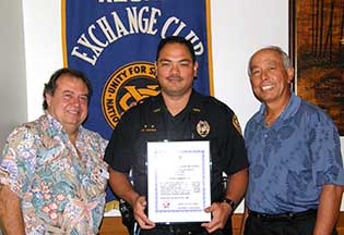 Photo: Officer Correa, holding a framed certificate stands between Chruchill and Estrell in front of the Exchange Club banner