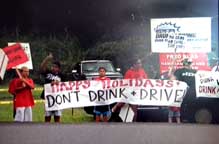 Image: community members wave signs advising motorists not to drink and drive.